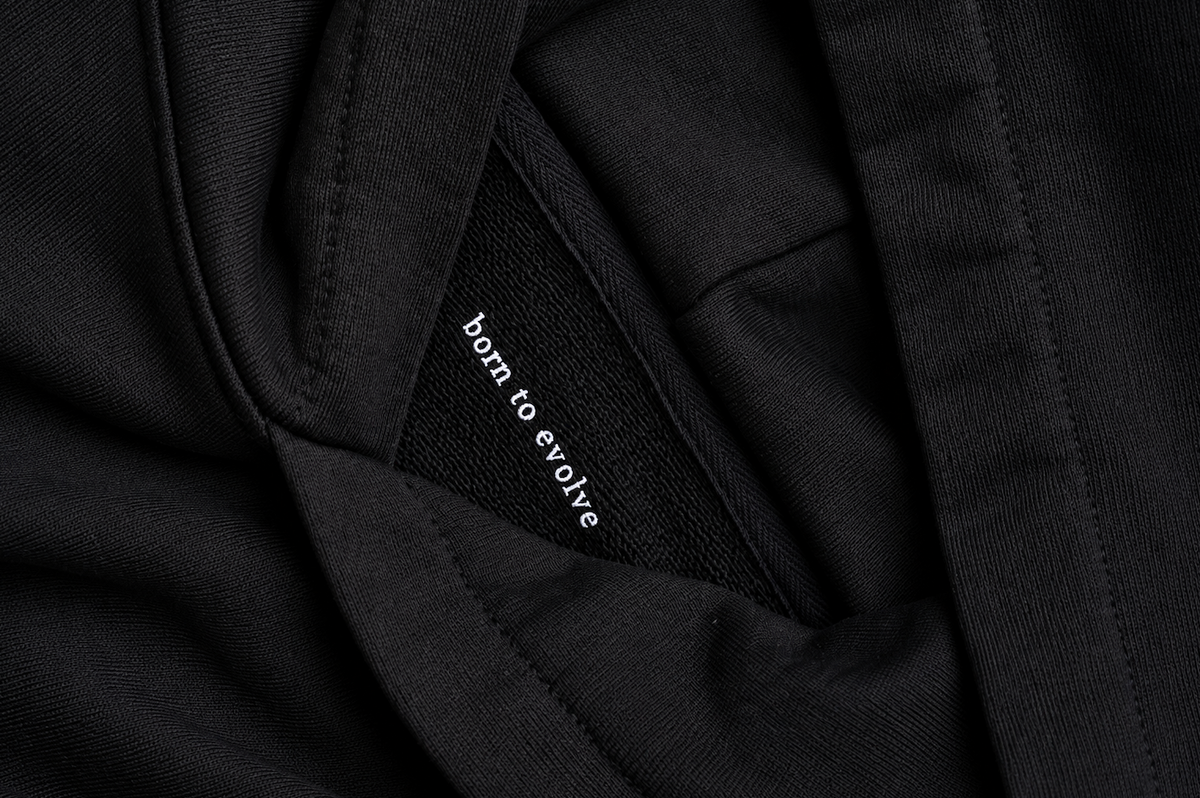 Close-up detail of the HUMÆ Founder Hoodie in Deep Black featuring the “born to evolve” message