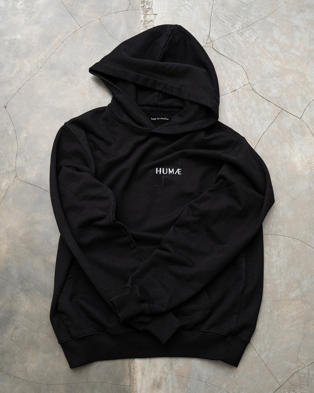 HUMÆ Founder Hoodie in Deep Black laid flat, featuring the embroidered HUMÆ chest logo