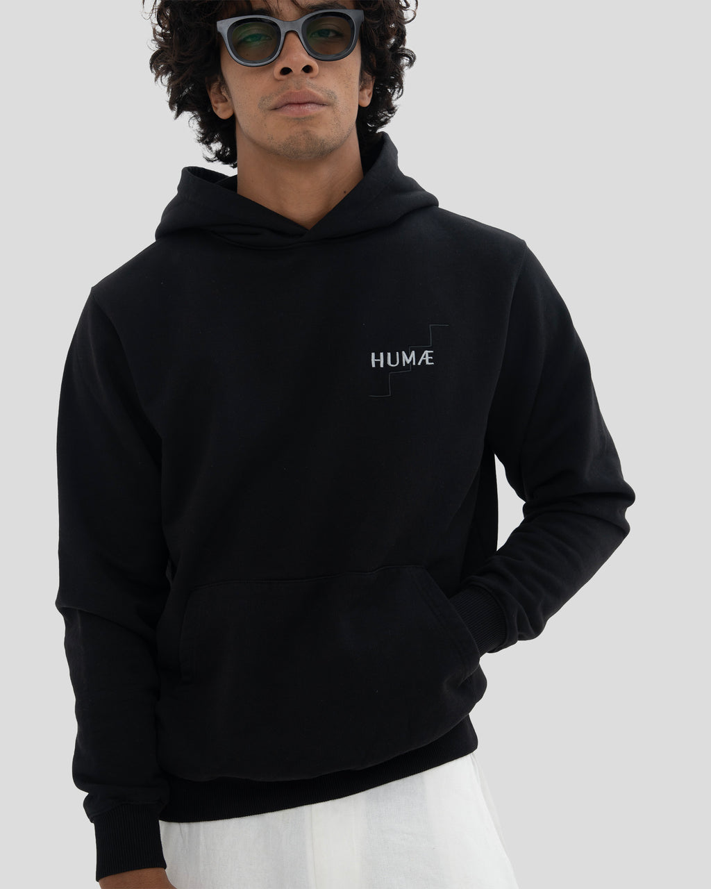 Man wearing the HUMÆ Founder Hoodie in Deep Black, standing front view with one hand in the pocket