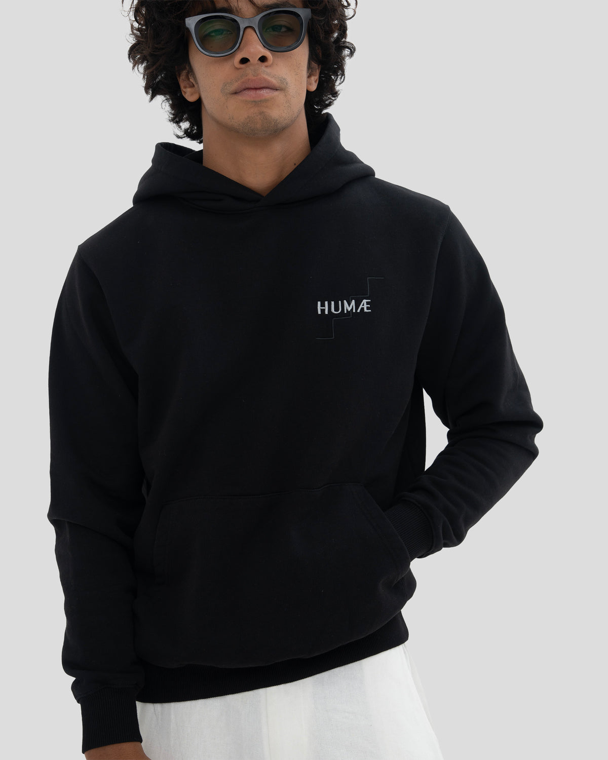 Man wearing the HUMÆ Founder Hoodie in Deep Black, standing front view with one hand in the pocket