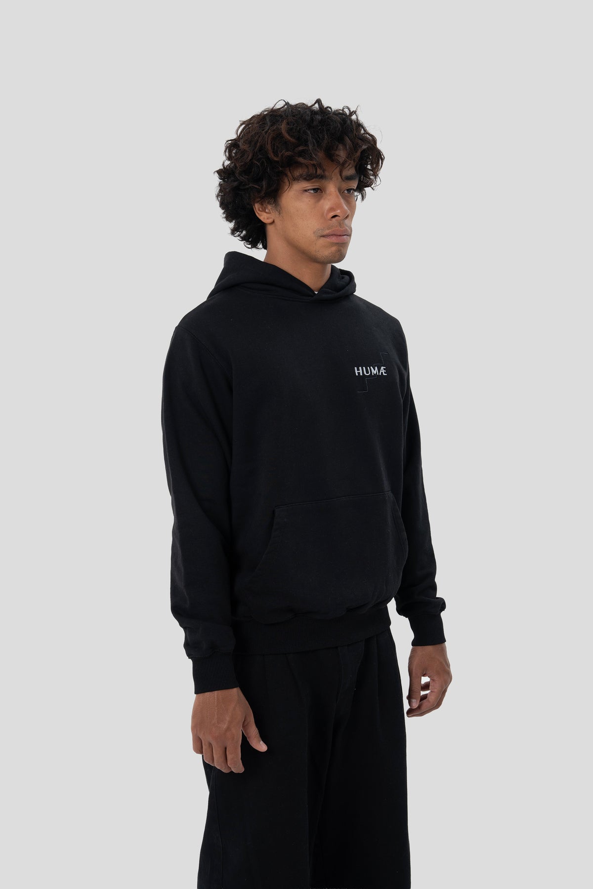 Man wearing the HUMÆ Founder Hoodie in Deep Black, shown in a three-quarter front view