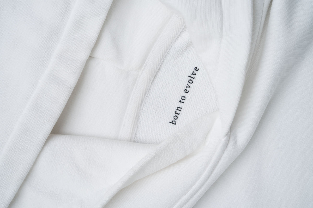 Close-up detail of the HUMÆ Founder Hoodie in Optical White featuring the “born to evolve” message