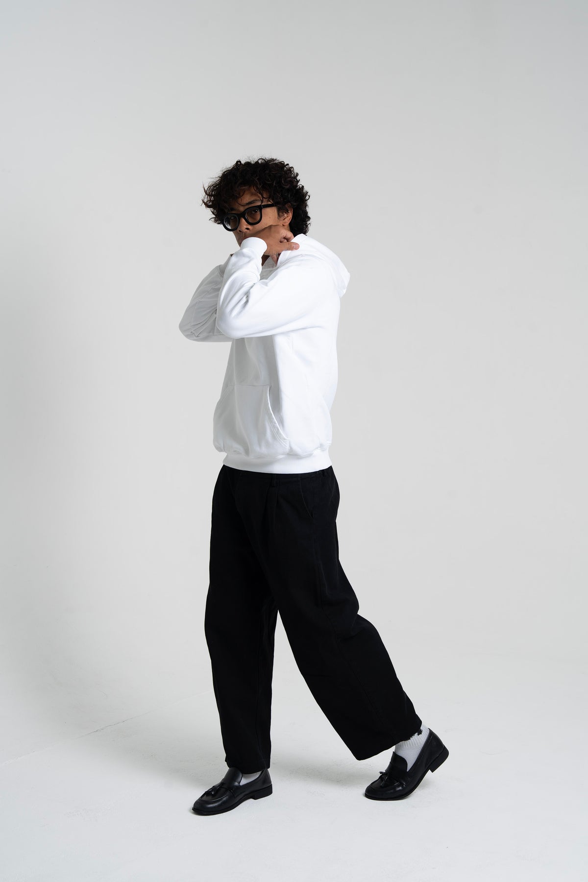 Man wearing the HUMÆ Founder Hoodie in Optical White with black trousers, shown in a dynamic full-body pose