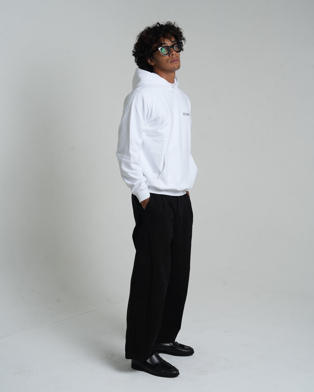 Man wearing the HUMÆ Founder Hoodie in Optical White, shown in a full-body side view with hands in pockets