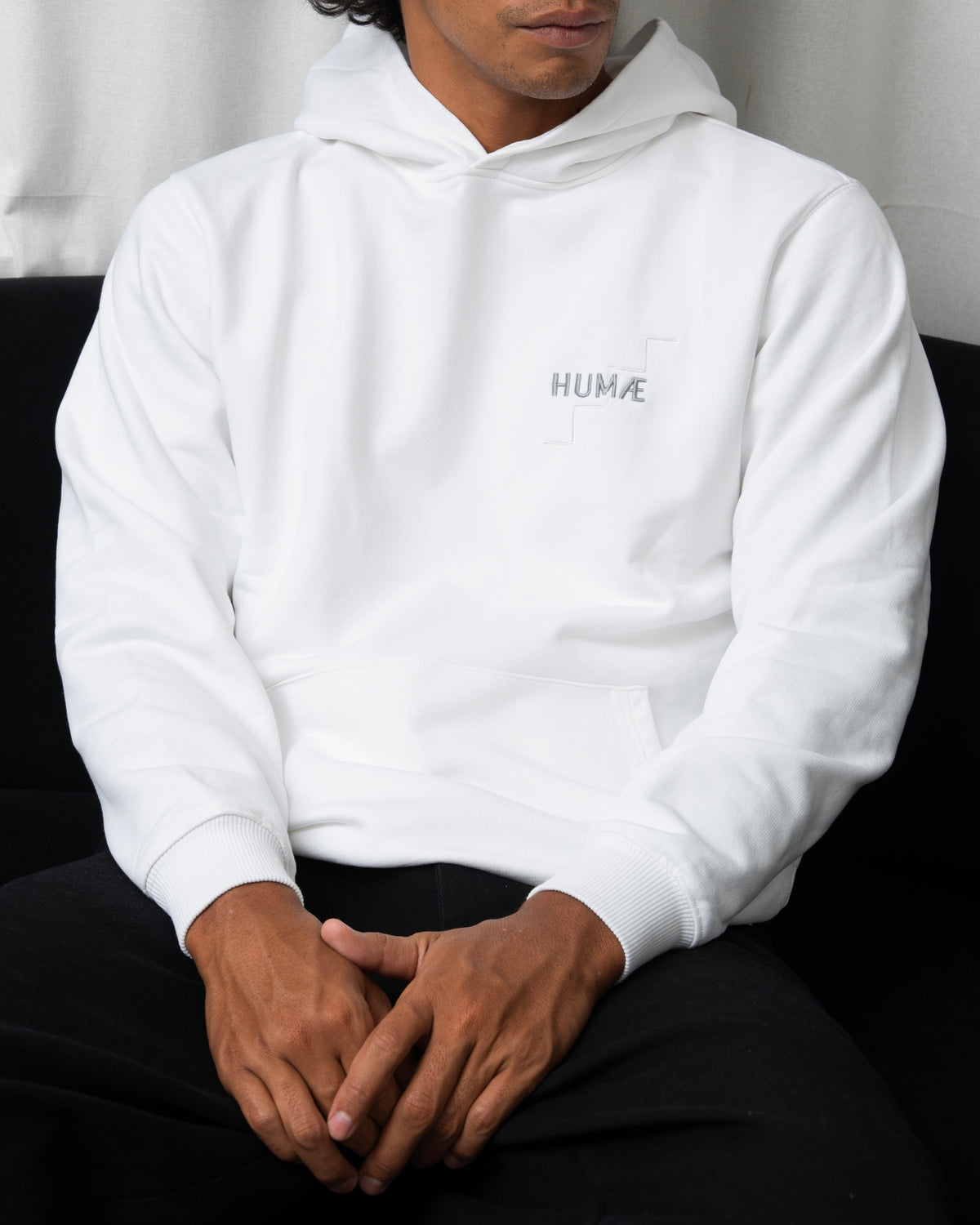 Man wearing the HUMÆ Founder Hoodie in Optical White, seated front view