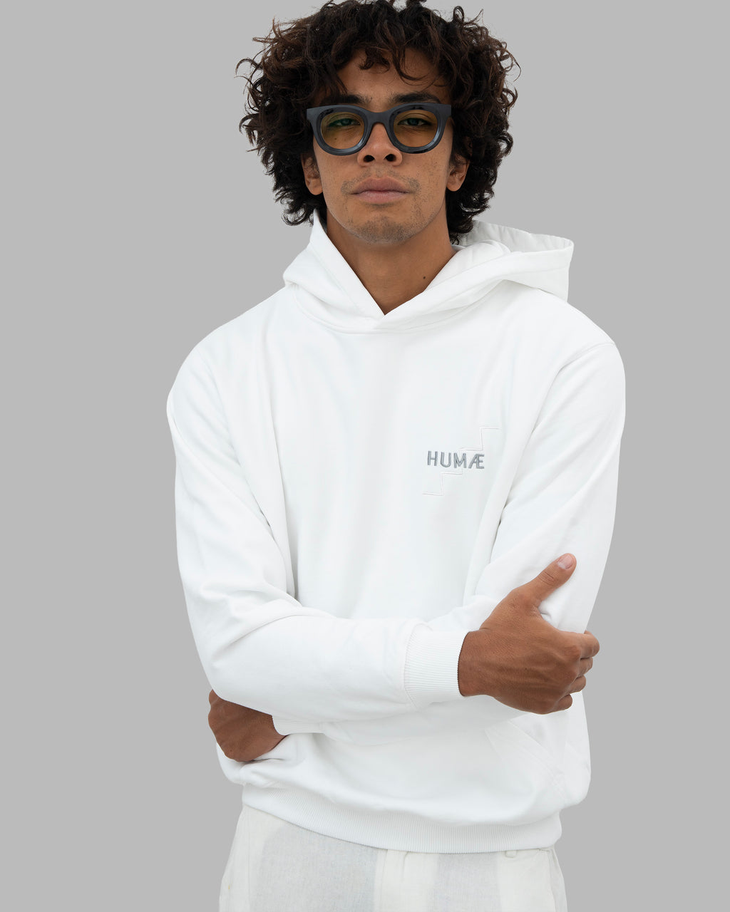 Man wearing the HUMÆ Founder Hoodie in Optical White, standing with arms crossed