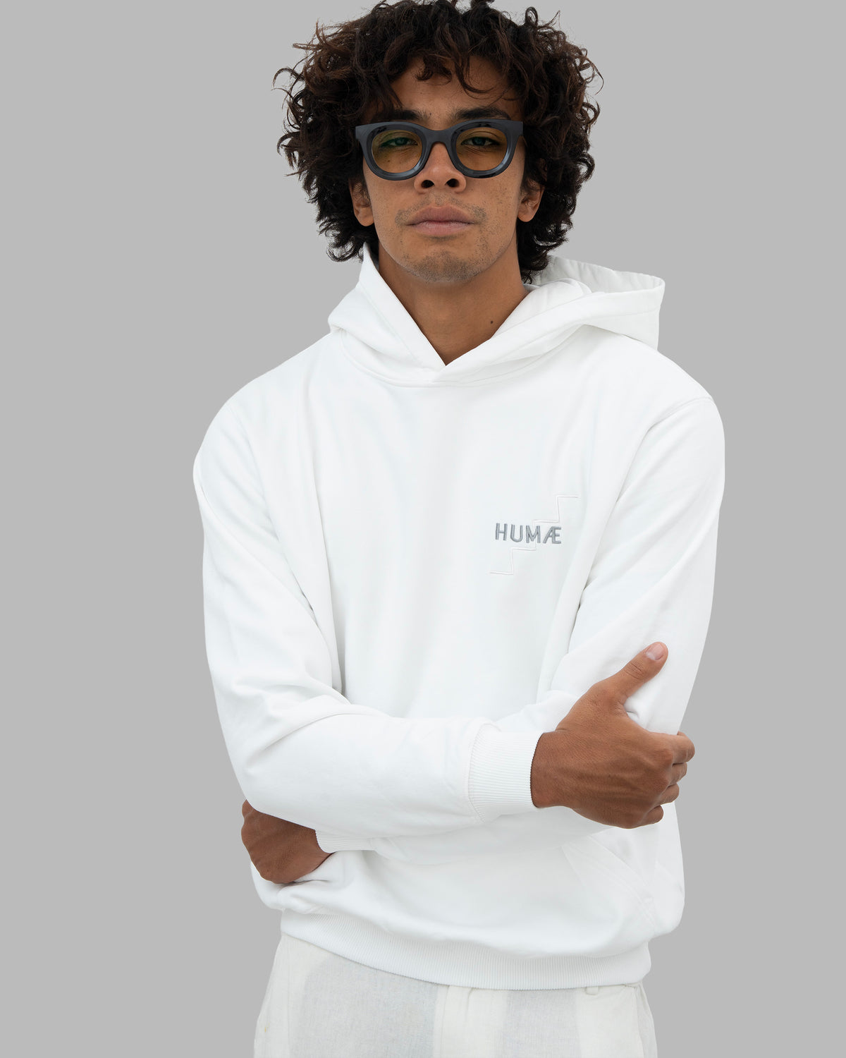 Man wearing the HUMÆ Founder Hoodie in Optical White, standing with arms crossed