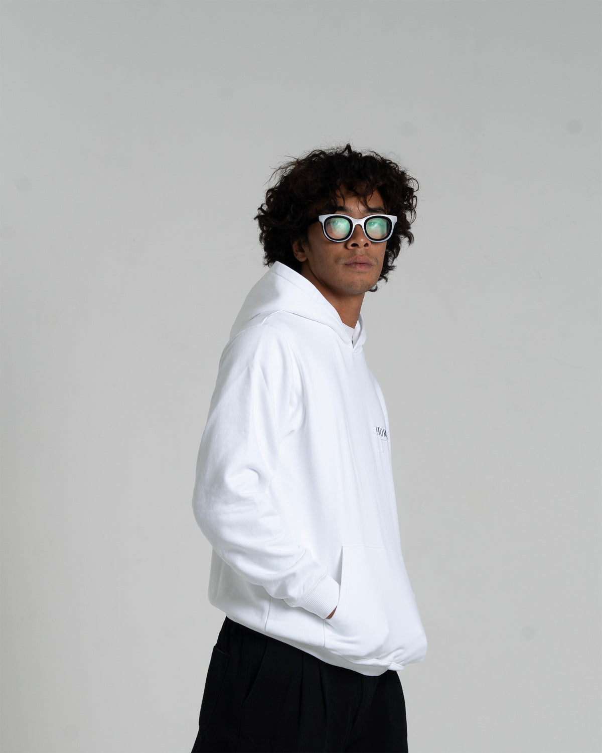 Man wearing the HUMÆ Founder Hoodie in Optical White, standing in side view with hands in pockets